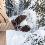 Brown sheepskin mittens worn with fuzzy cuffs, dusted with snow outdoors